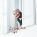 An older lady is looking out of a window at the camera