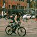 someone is seen cycling on a road in a city they are wearing a helmet and a backpack