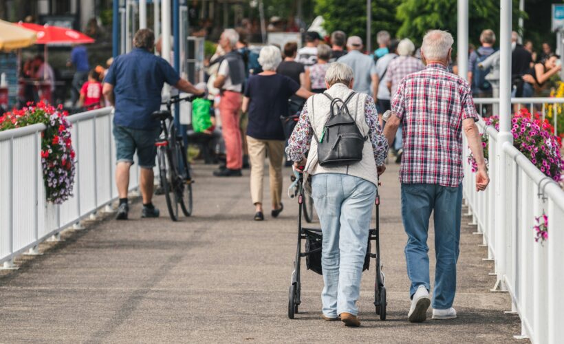 Two people are walking on a crowded street one with a walker to represent pain awareness month 2025