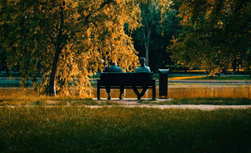 Two people seen from a distance talking on a bench. All around them are beautiful trees in autumnal colours to represent world suicide prevention day