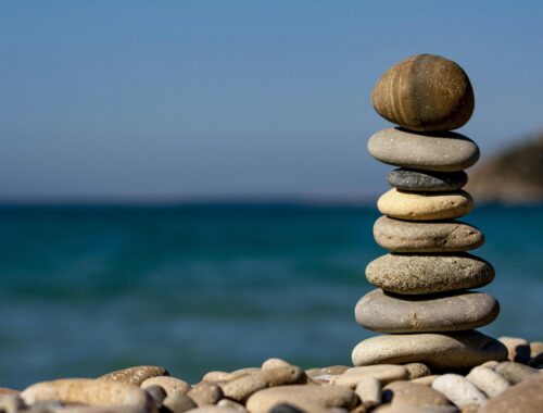 A pile of stones are seen on a beach with blue skies and the sea behind