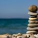A pile of stones are seen on a beach with blue skies and the sea behind
