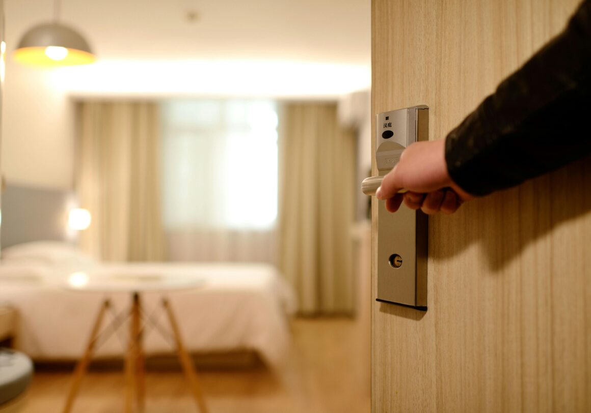 A person's hand is seen on an open doorhandle leading into a beautiful hotel room