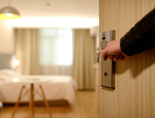 A person's hand is seen on an open doorhandle leading into a beautiful hotel room