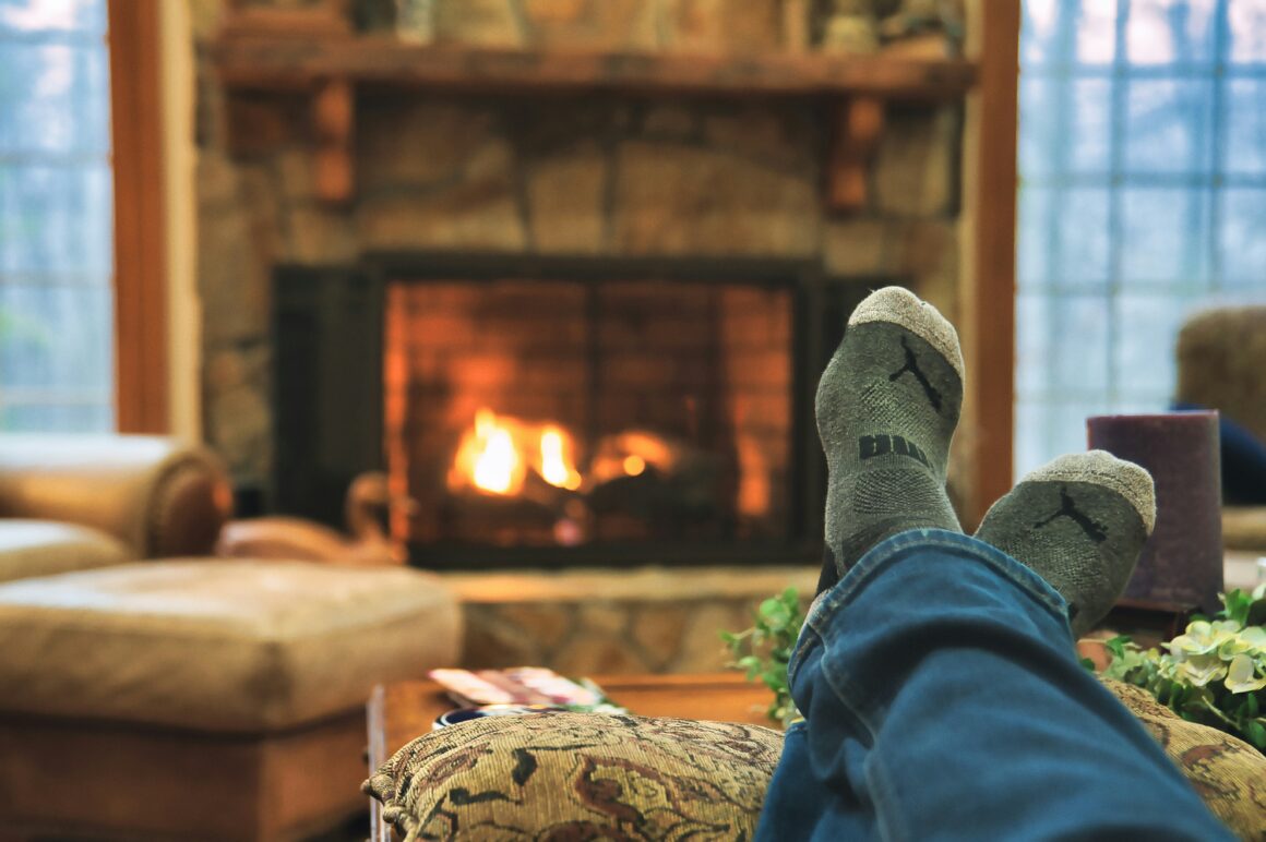 We see someone with cosy socks, their feet up in front of a roaring fire it is a cosy scene to represent How Late Winter Affects My Mental Health