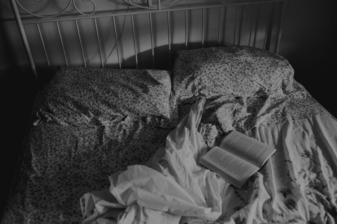 A messy bed is seen from above in black and white, on the bed lays an open book to represent a gentle routine for flare days