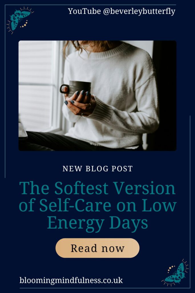 A person is seen sitting in a window, they are wearing a cosy jumper and are holding a mug of hot drink in their hands to represent The Softest Version of Self-Care on Low Energy Days