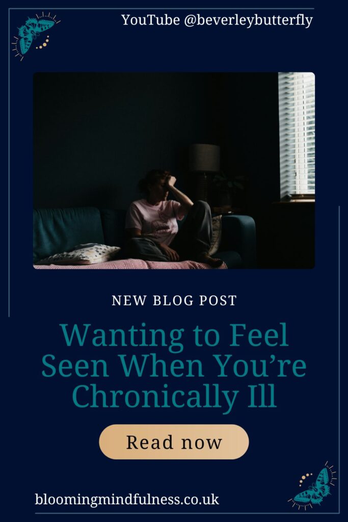 A person is seen sitting on a sofa near a window, they are curled up with their head in their hands and they are in low light to represent Wanting to Feel Seen When You’re Chronically Ill