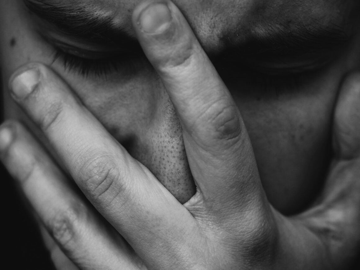 A man is seen, in black and white, with a hand over his face clearly struggling.
