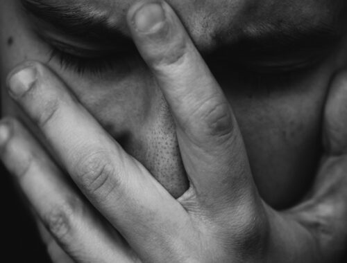 A man is seen, in black and white, with a hand over his face clearly struggling.