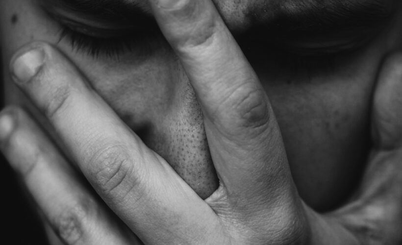 A man is seen, in black and white, with a hand over his face clearly struggling.