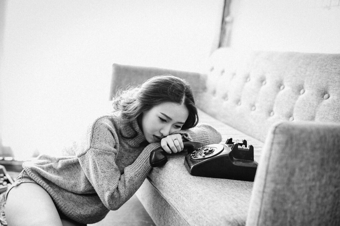 A woman is seen leaning on a sofa crying, beside her is a telelphone and the picture is black and white to represent The Trauma of Being Misdiagnosed