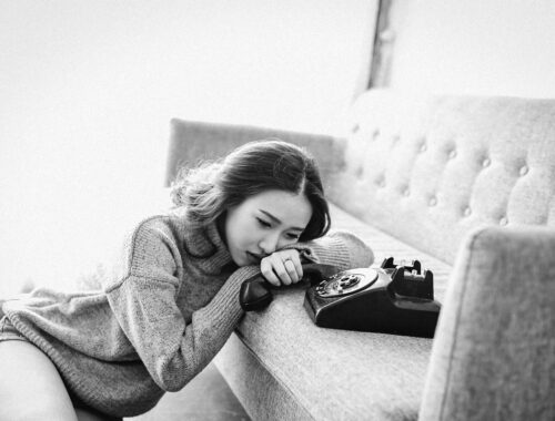 A woman is seen leaning on a sofa crying, beside her is a telelphone and the picture is black and white to represent The Trauma of Being Misdiagnosed
