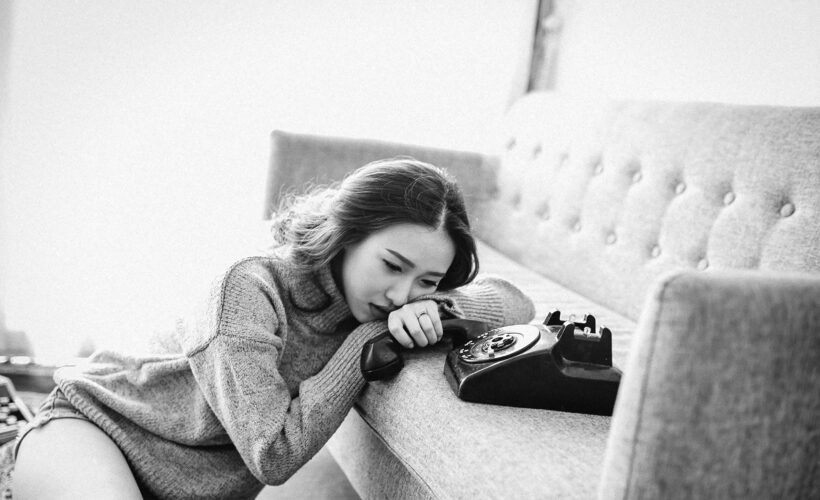 A woman is seen leaning on a sofa crying, beside her is a telelphone and the picture is black and white to represent The Trauma of Being Misdiagnosed